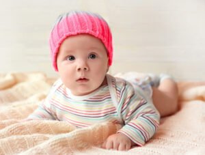 Este bebé está encima de la cama. Lleva puesto un pañal y un gorro de lana de color rosa.