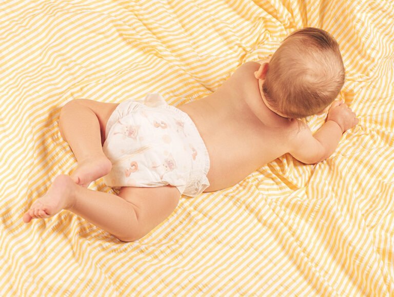 Bebé con pañal puesto encima de la cama. La funda nórdica es de rayas blancas y amarillas.