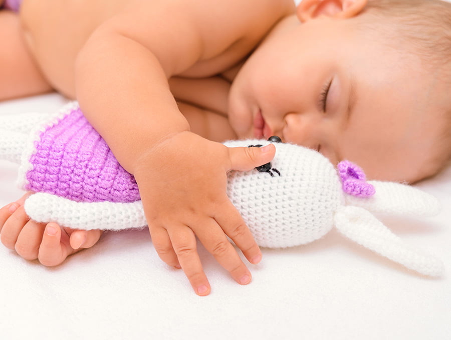 Este bebé está durmiendo la siesta tranquilamente en su cama. Tiene un muñeco de trapo entre sus manos.
