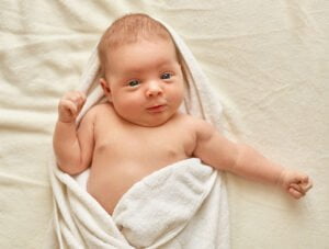 Este bebé ha salido del baño. Ahora está envuelto con una toalla blanca de algodón para secarse. Está encima de la cama de sus padres.