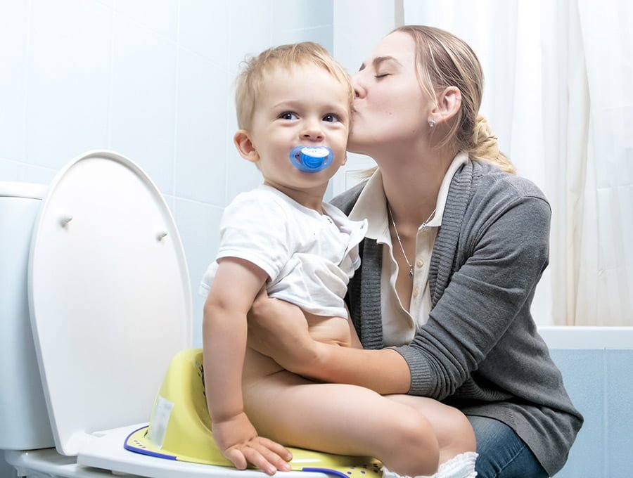 Esta madre está enseñando a su hijo a utilizar el water del cuarto de baño. Lo ayuda a sujetarse.