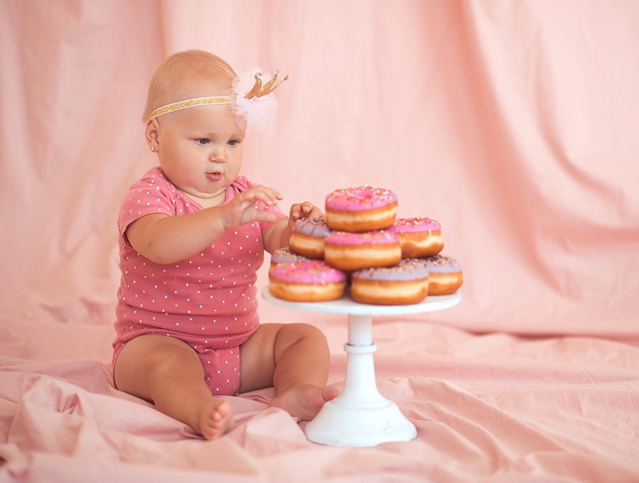 Una niña pequeña junto a un montón de donuts de chocolate de fresa.