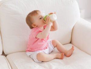 Este bebé se está tomando el biberón de leche encima del sofá del comedor.
