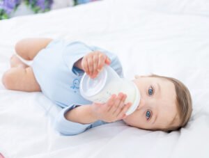 Este bebé se está tomando el biberón de leche de continuación encima de la cama de sus padres.