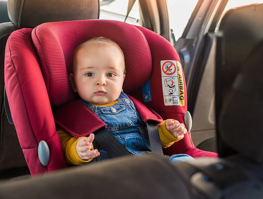 Este bebé está sentado en una sillita para el coche adaptada a niños pequeños y fijada al asiento del vehículo.