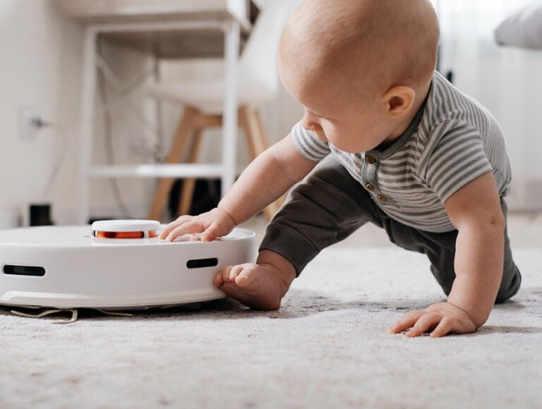Este bebé está tocando el robot aspirador que pasa por la alfombra. Estos robots aspiradores son muy silenciosos.