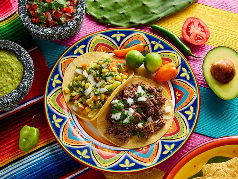 Mesa con mantel de colores. Encima hay distintos platos de comida mexicana con mucho pique.