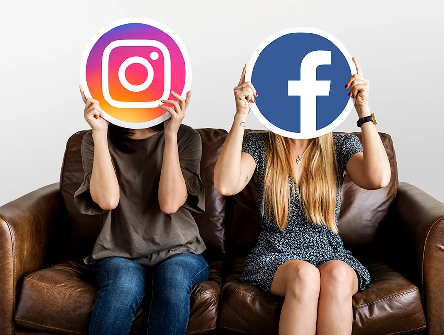 Estas dos mujeres están sentadas en un sofá de piel. Ambas sujetan un logo de la red social. Uno de instagram y otro de facebook.