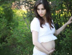 Mujer embarazada ha salido a dar una vuelta por el bosque. Ahora está parada junto a un arbol.