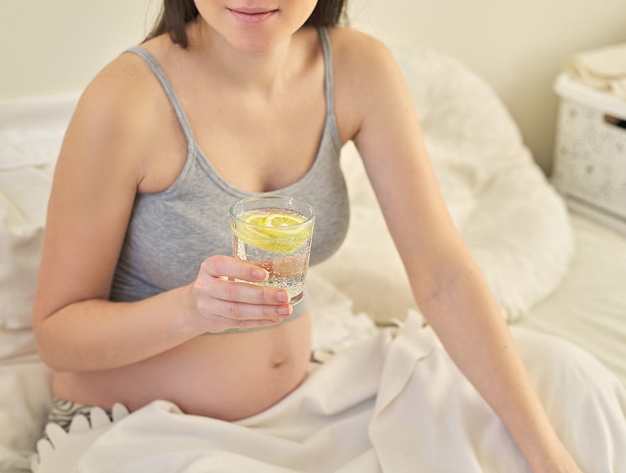 A esta embarazada se le ha antojado tomar un poco de agua con gas y unas rodajas de limón. Está descansando en la cama.