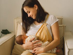 Esta madre está sentada en un sillón dándole el pecho a su bebé recién nacido.