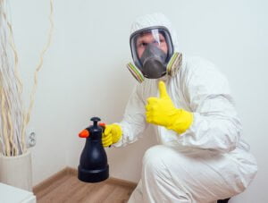 Este hombre lleva un traje EPI mientras pulveriza spray anti pulgas en los rincones de su casa.