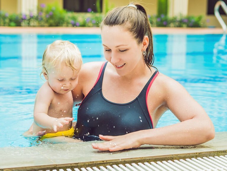 Esta madre en bañador está dentro de la piscina con su hijo pequeño, que lleva un pañal para nadar.