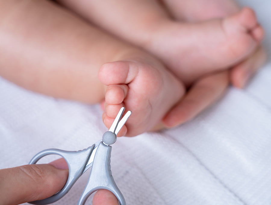 Esta madre le va a cortar las uñas de los pies a su hijo recién nacido con unas tijeras de punta redonda.
