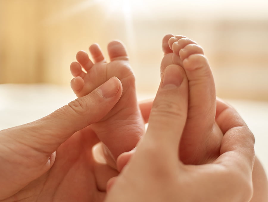 Esta madre le está juntando un poco de crema corporal de bebés en los pies de su recién nacido.