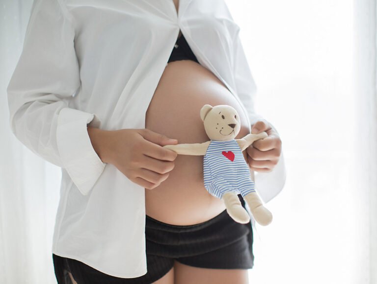 Esta embarazada sostiene un peluche de un osito junto a su gran barriga.