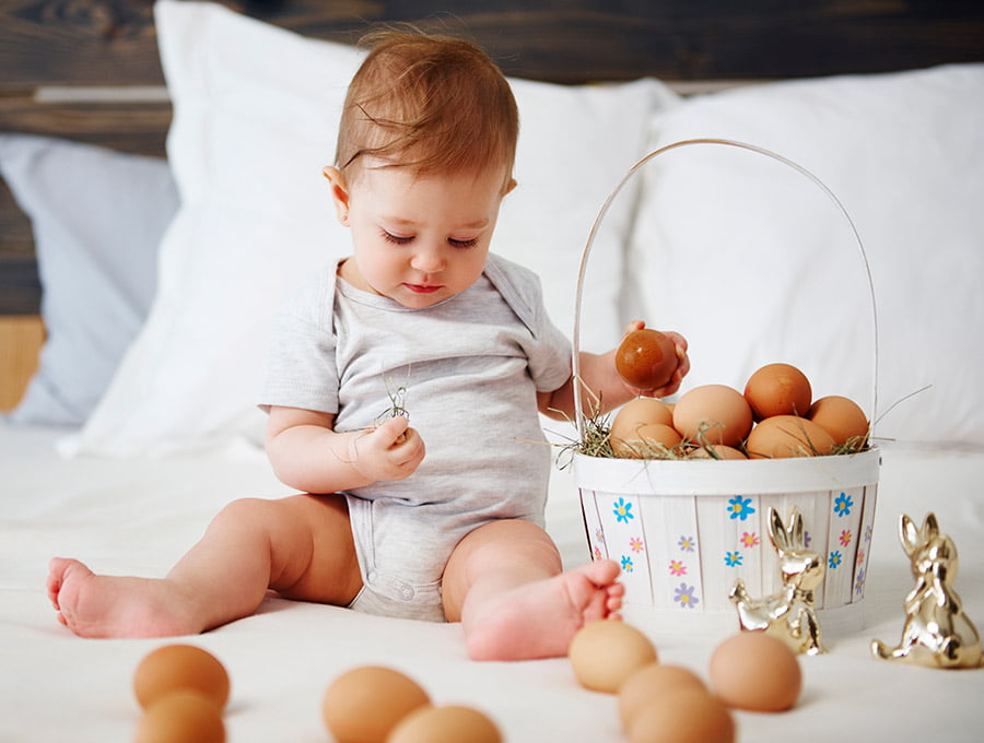 Este niño pequeño está encima de la cama. Hay muchos huevos de gallina en la cesta, también por la cama.