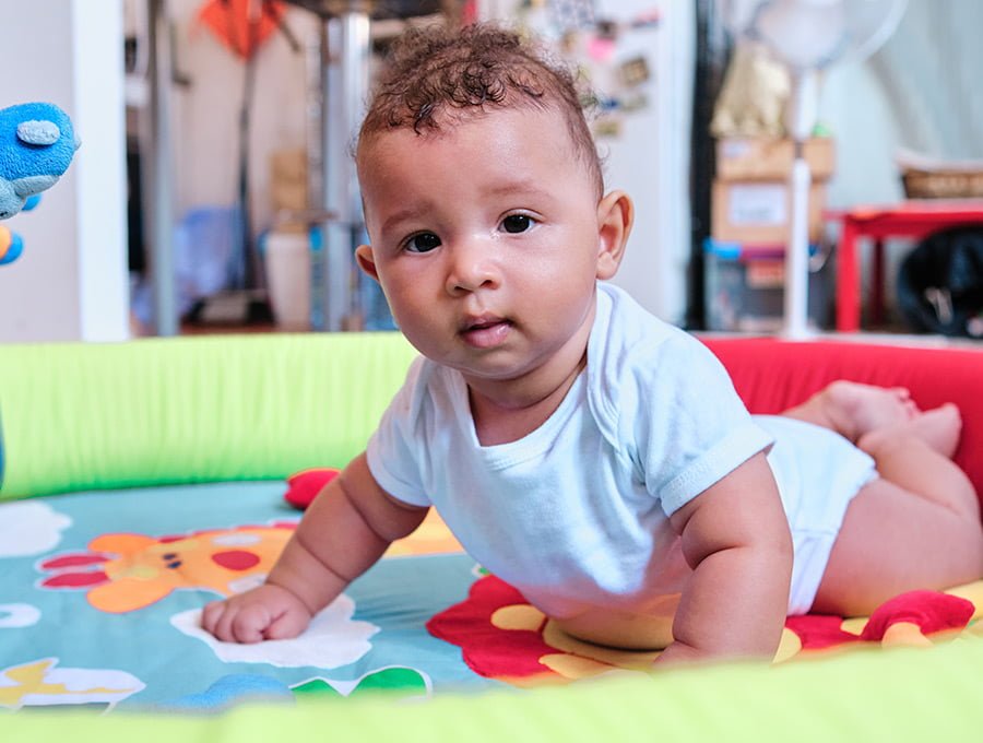 Este bebé está jugando encima de una alfombra infantil de colores.