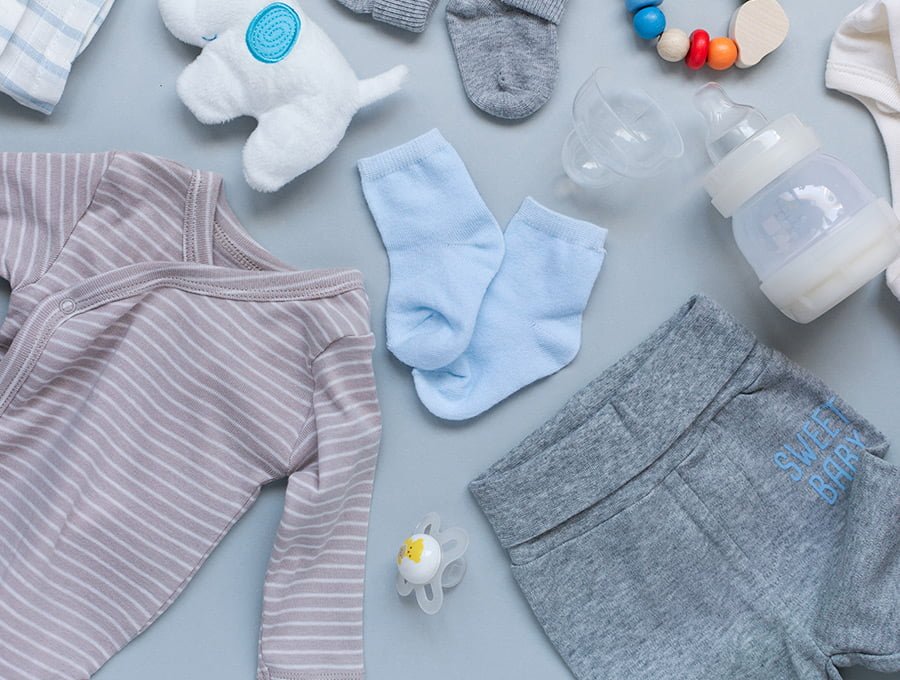 Varias prendas de vestir de bebé. También hay otros artículos de cuidados infantiles (biberón, sonajero)