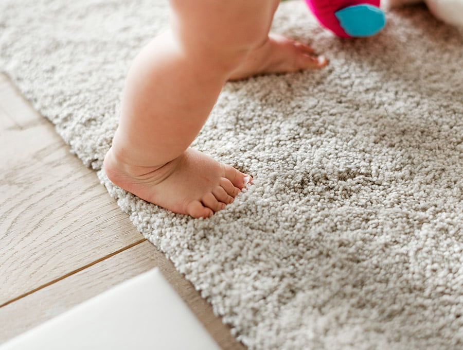 Este bebé está aprendiendo a caminar sobre la alfombra del salón.