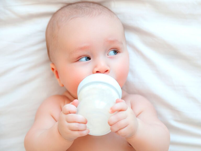 Este bebé está mirando entusiasmado a un lado mientras se bebe la leche del biberón.