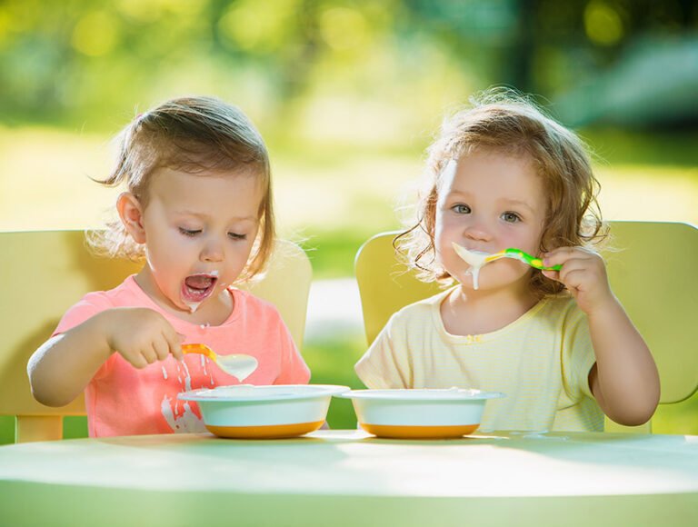 Estas dos niñas pequeñas están sentadas en la mesa del jardín. Están disfrutando de una deliciosa papilla de cereales.