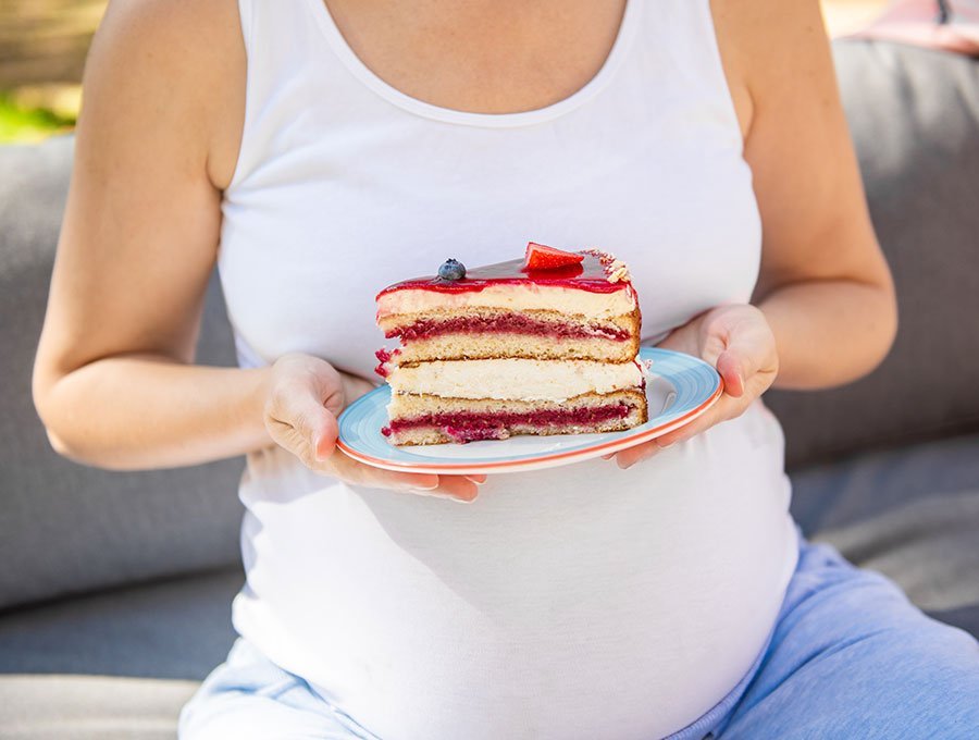 Esta embarazada tiene en sus manos un plato con un trozo grande de pastel de fresa y queso.