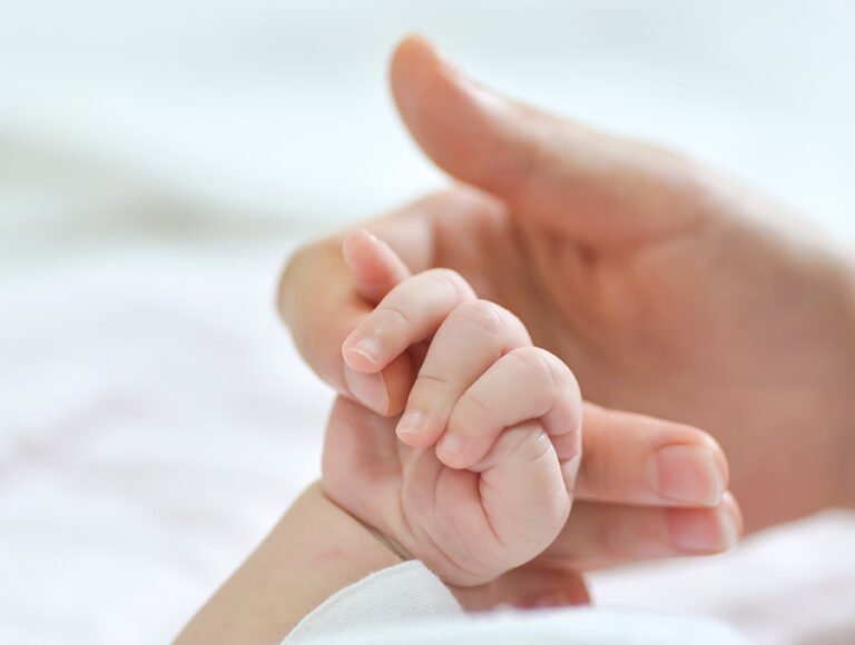 Esta madre está tocando la mano pequeñita de su bebé recién nacido.