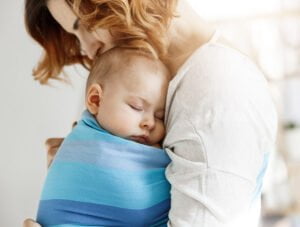Esta madre tiene a su bebé cogido en brazos, le está dando un beso en la cabeza. El pequeño está dormido.