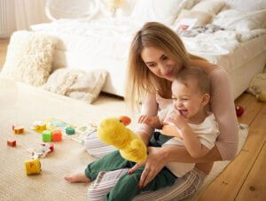 Esta madre juega con su bebé y sus juguetes en la alfombra del salón.