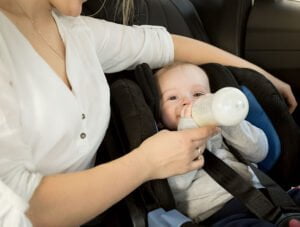 Esta madre le está dando el biberón de leche a su bebé mientras están de viaje en el coche.