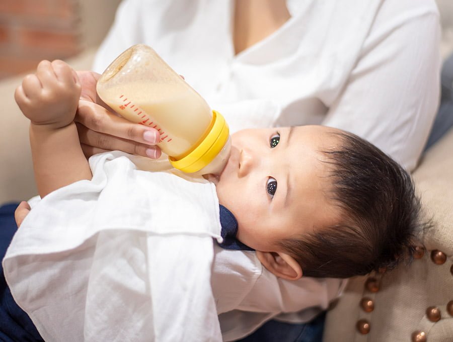 Este niño se está tomando la leche en un biberón de plástico. La madre tiene al bebé cogido en brazos.