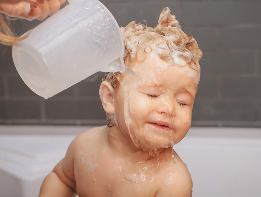 Esta madre le está enjuagando la cara con agua a su hijo pequeño. Se estaba bañando y le ha llegado jabón a los ojos.