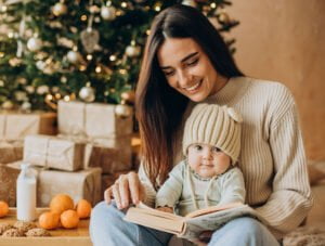 Esta madre le está leyendo un cuento a su bebé junto al arbol de Navidad.