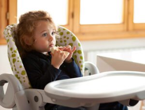 Esta niña está comiendo pan sentada en su trona. Está muy concentrada comiendo.