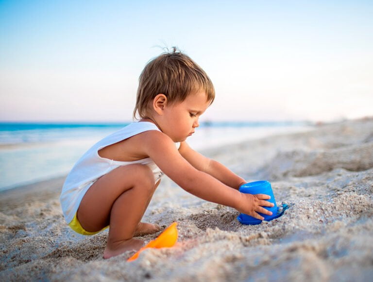 Este niño está jugando con su cubo azul y la arena de la playa.