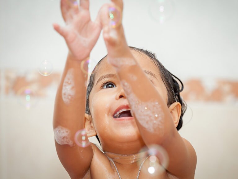 Este niño pequeño está jugando con la espuma y las pompas de jabón durante el baño.