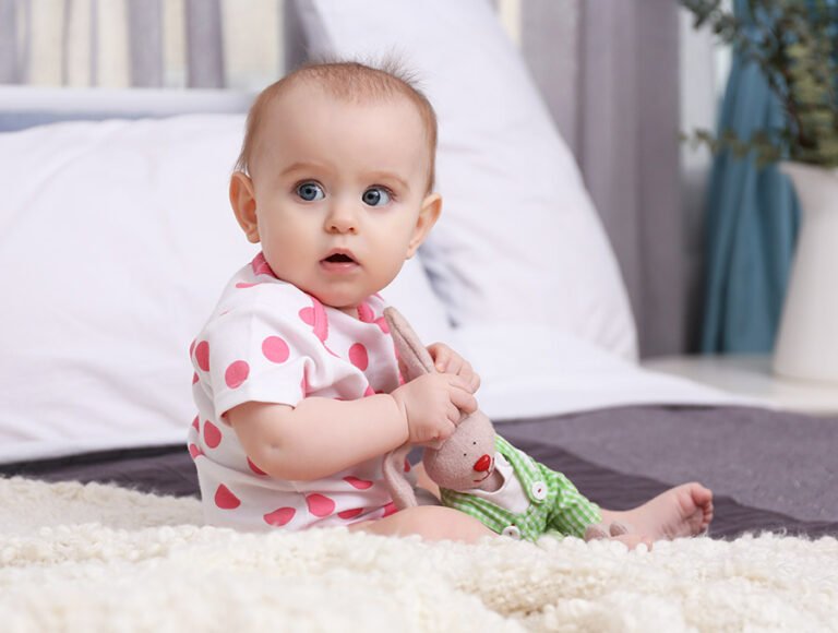 Este bebé está entretenido jugando con el peluche encima de la alfombra del salon.