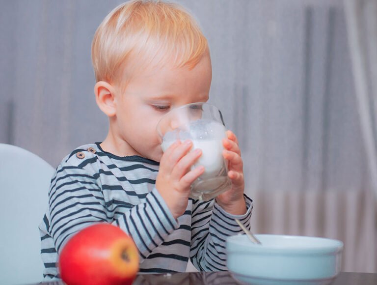 Este niño pequeño está sentado en la silla de la cocina tomándose un vaso de leche.