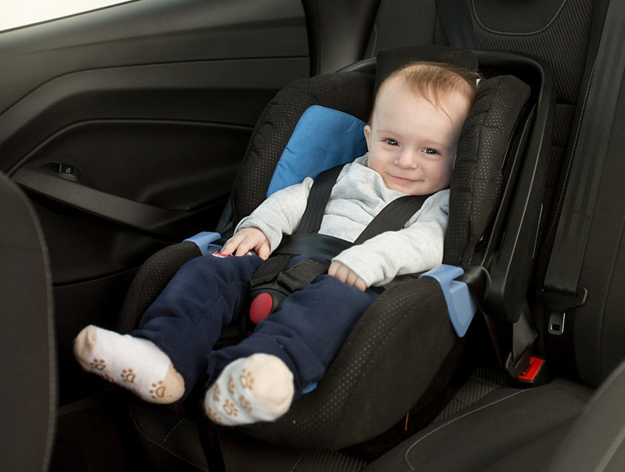 Este niño pequeño está bien sujeto en la silla del coche. Se está medio riendo.