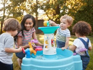 Estos tres niños juegan con su madre y la mesa de agua en el jardín. Parece que disfrutan.