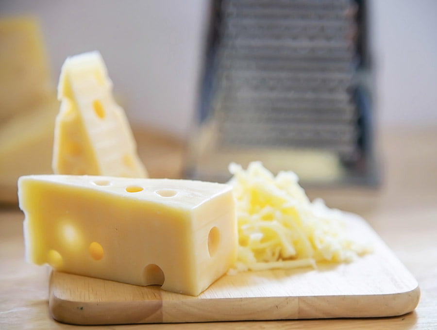 Dos trozos de queso y queso rallado sobre una tabla de cortar de madera.
