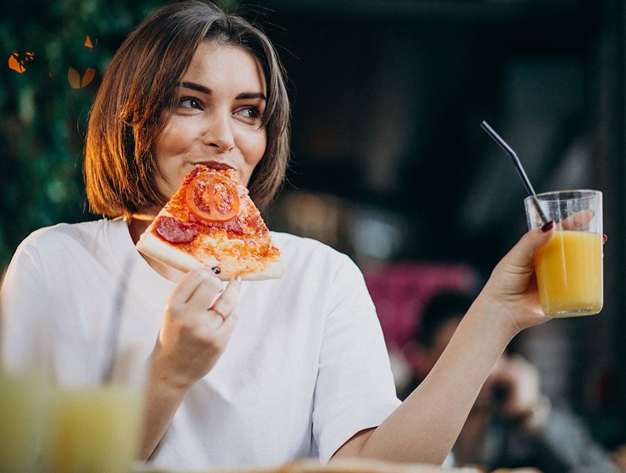Esta mujer está comiendo una porción de pizza del Dómino´s con un zumo de naranja natural.