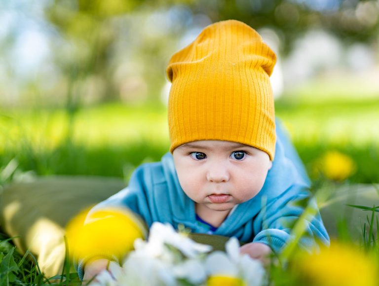 Bebé pequeño con gorrito y ropa azul, jugando sobre el césped del jardín.