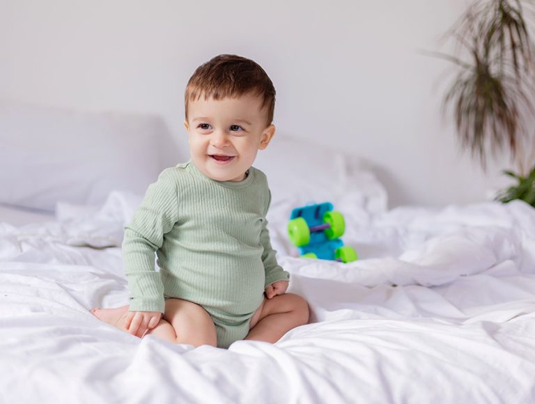Bebé jugando con un cochecito de plástico encima de la cama de sus padres.