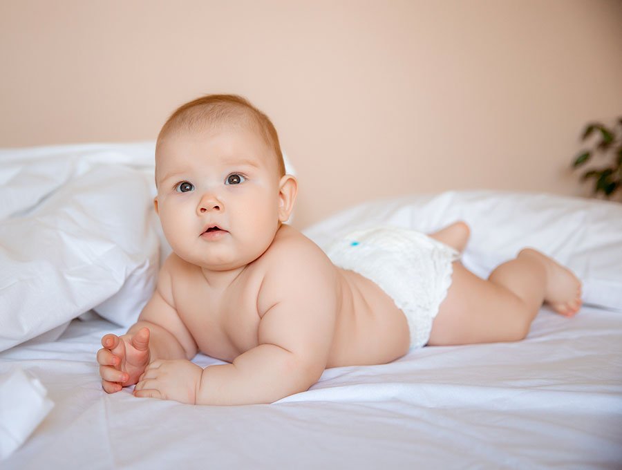 Bebé regordete con pañal encima de la cama de sus padres.
