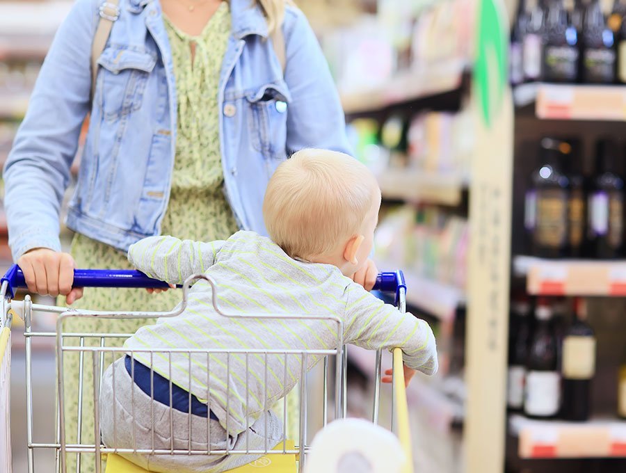 Niño sentado en el carrito de la compra mientras la madre compra en el supermercado.